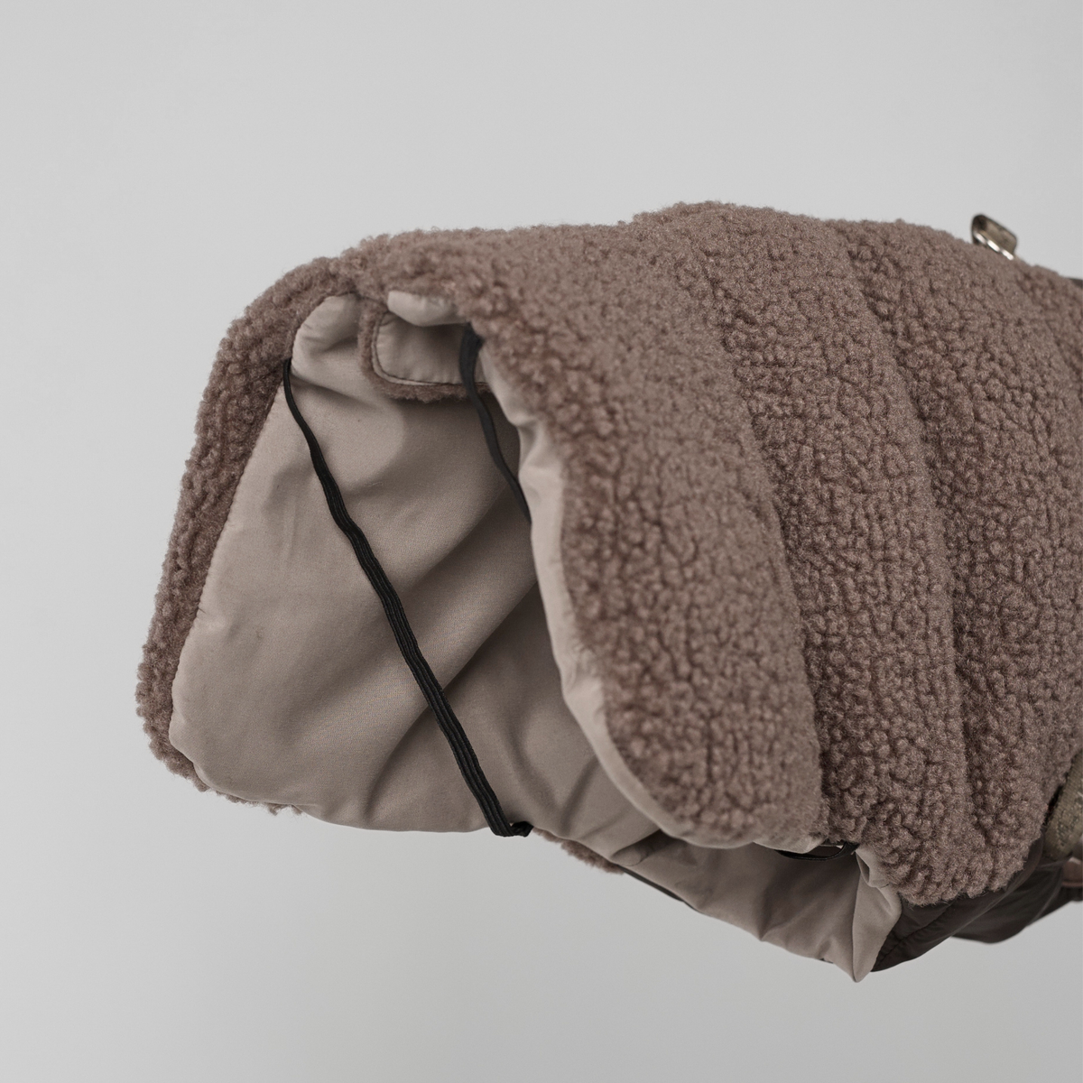 De taupe teddyhondenjas is opgerold, waardoor de voering zichtbaar is