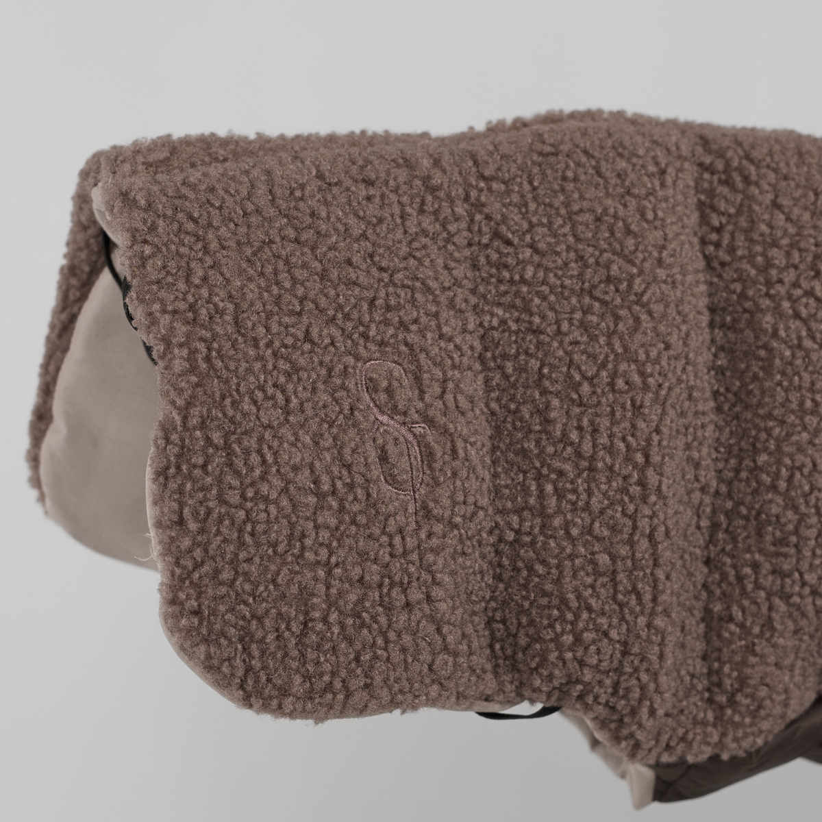 Close-up van het in reliëf aangebrachte Staey-monogram op het taupe-kleurige teddyhondenjas