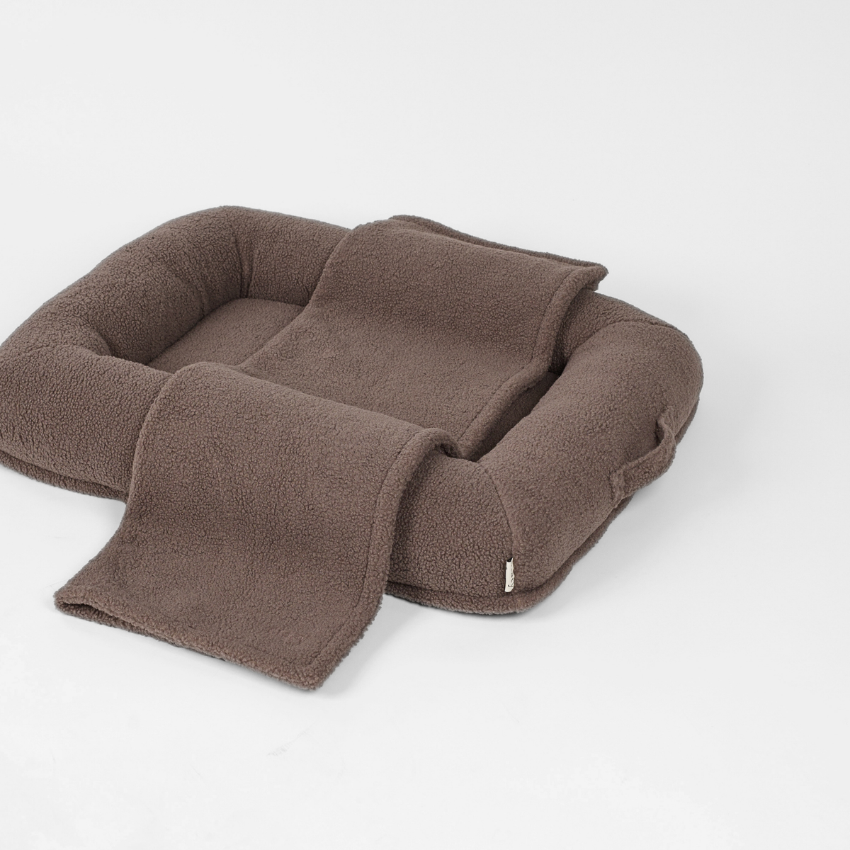 De taupe teddy-hondenmand met een bijpassend dekentje dat over de rand hangt